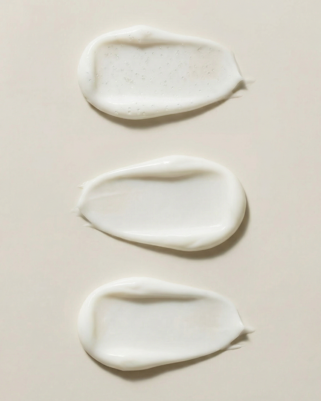 Three droplets of white cream on a beige background